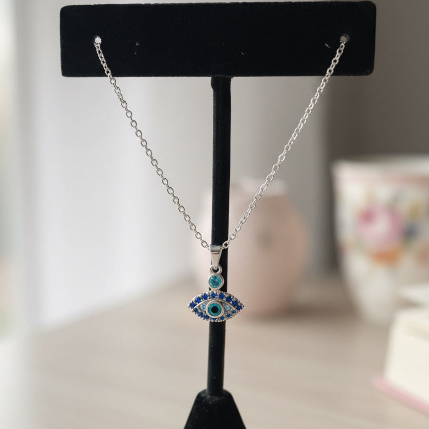 Silver necklace with a blue evil eye pendant on a black stand against a blurred background