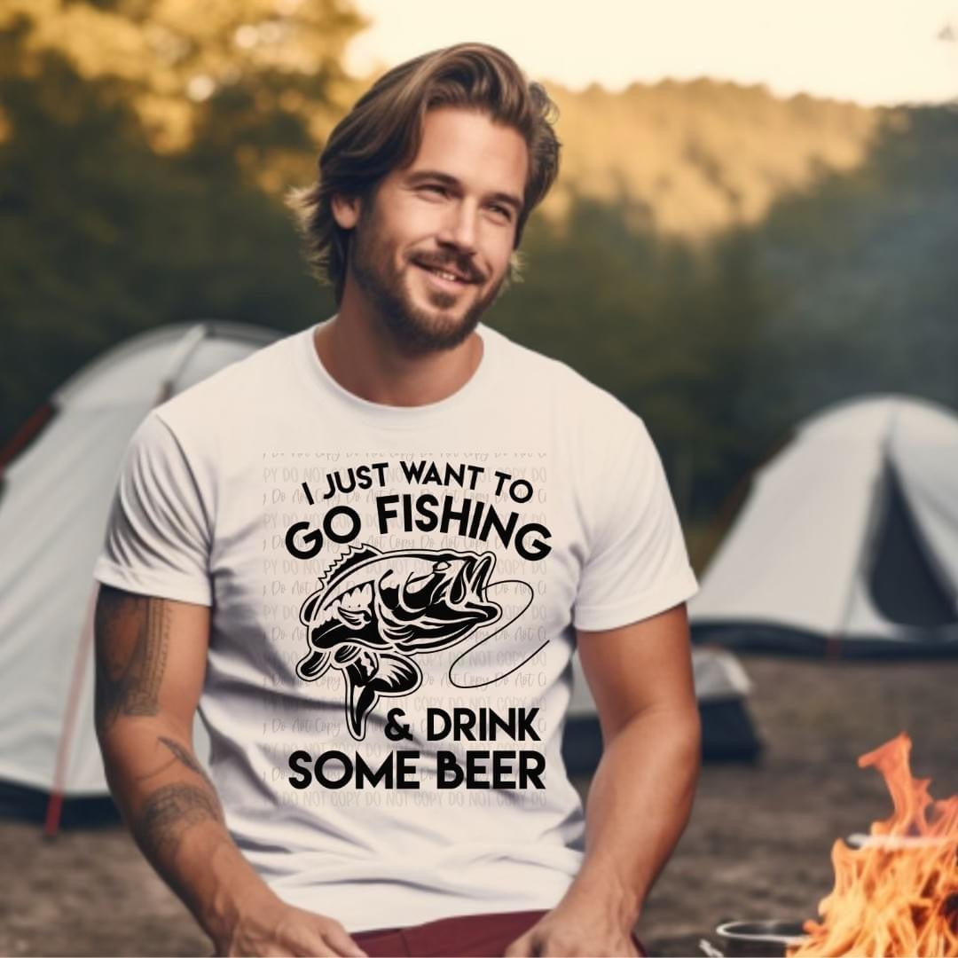 Man wearing a t-shirt with a fishing and beer graphic, sitting by a campfire with tents in the background.
