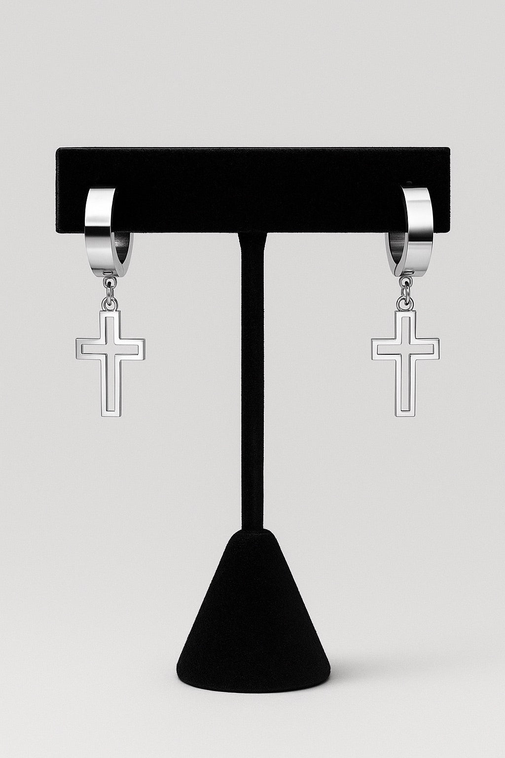 Silver hoop earrings with cross charms on a black stand against a light gray background