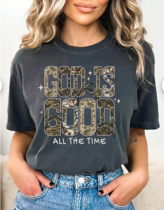 Person wearing a grey/black t-shirt with 'God is Good All the Time' text and camouflage design.