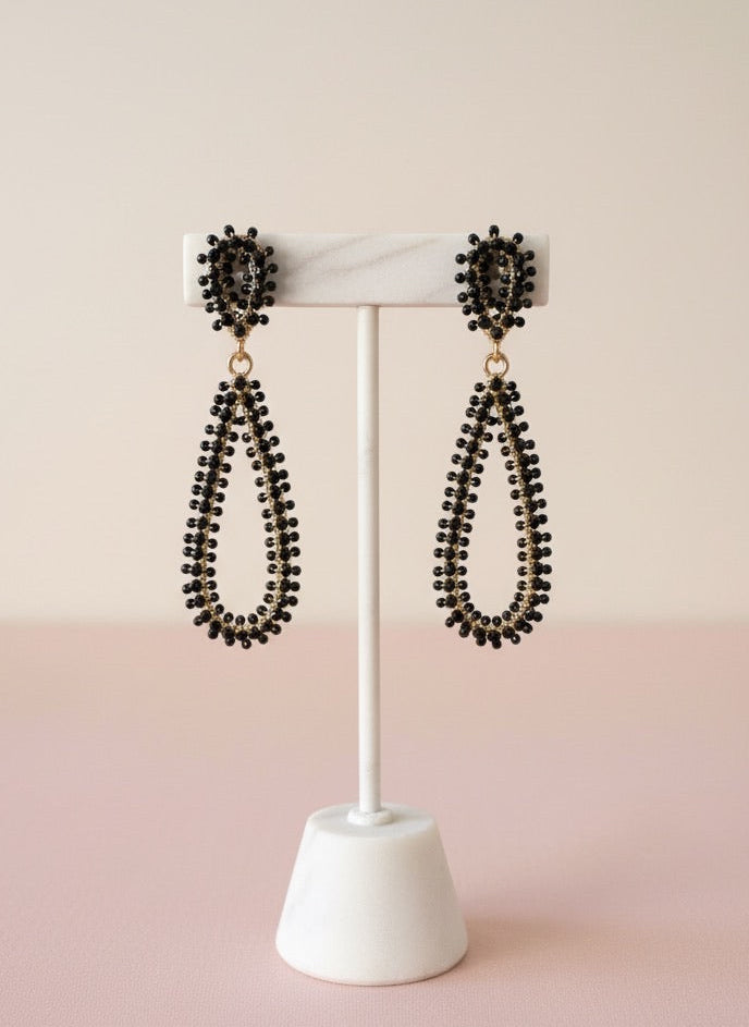 Pair of black beaded earrings on a white stand against a pink background