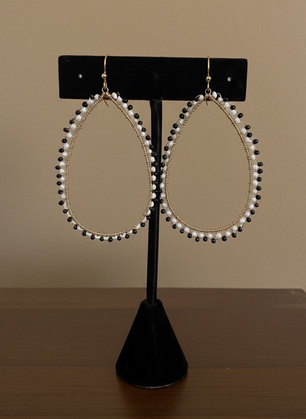 Pair of pearl like hoop earrings on a black display stand against a beige background