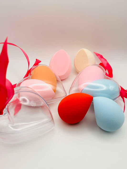 Set of colorful makeup sponges with a clear heart container on a white background