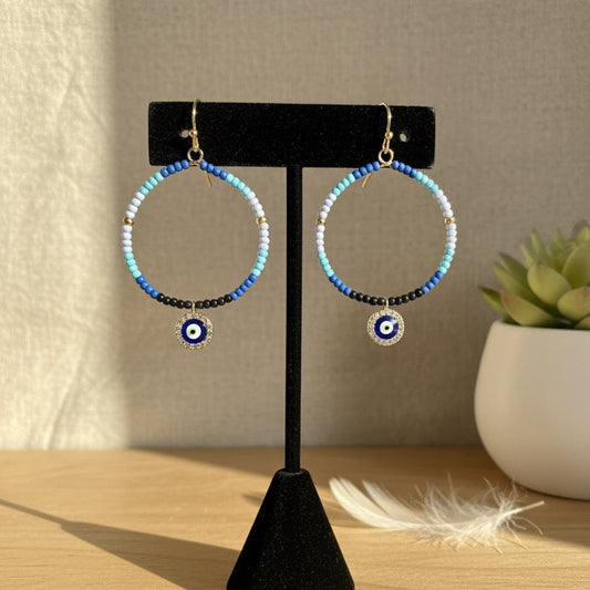 Pair of blue beaded hoop earrings with a central evil eye design on a black stand.
