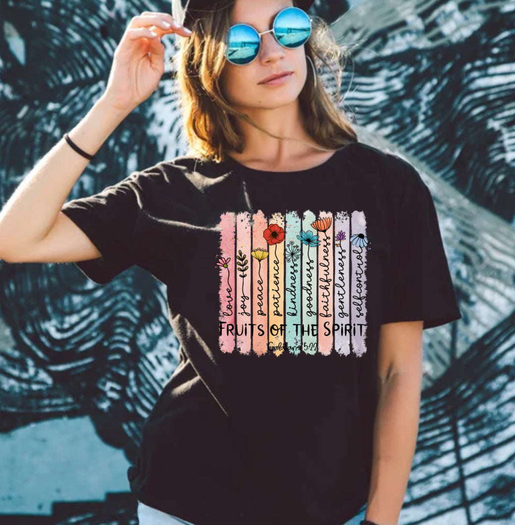 Person wearing a black t-shirt with colorful graphics and text, standing against a textured wall.