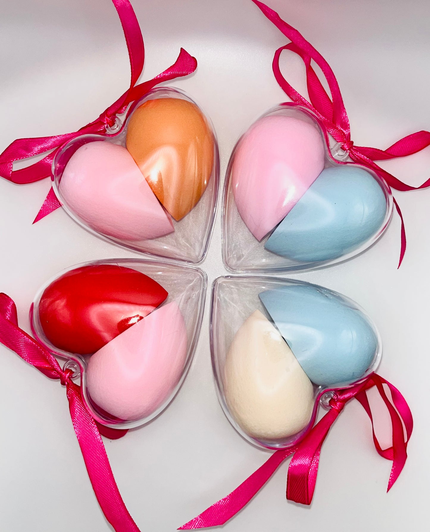 Heart-shaped containers with colorful half-oval beauty blenders and pink ribbons on a white background