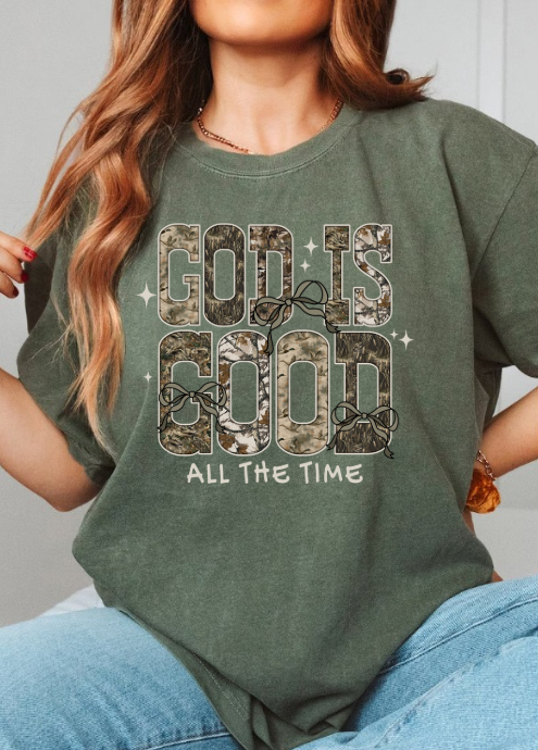  Person wearing a olive green t-shirt with 'God is Good All the Time' text in camouflage design. 
