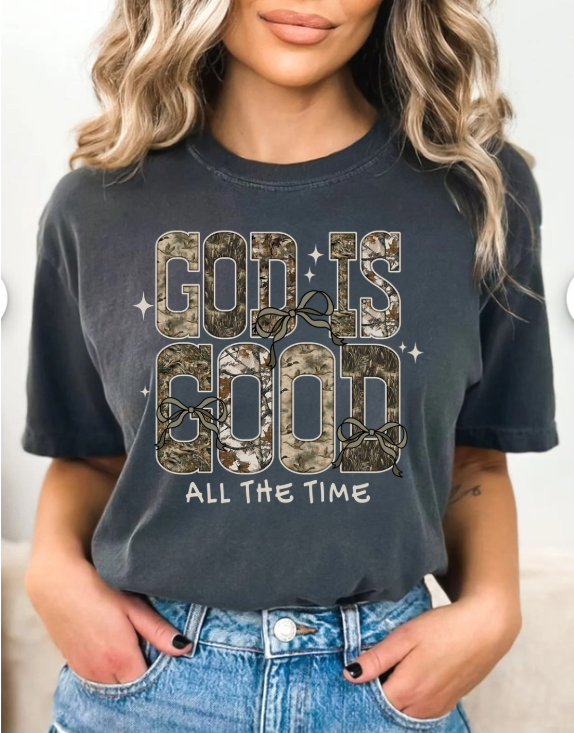 Person wearing a grey/black t-shirt with 'God is Good All the Time' text and camouflage design.