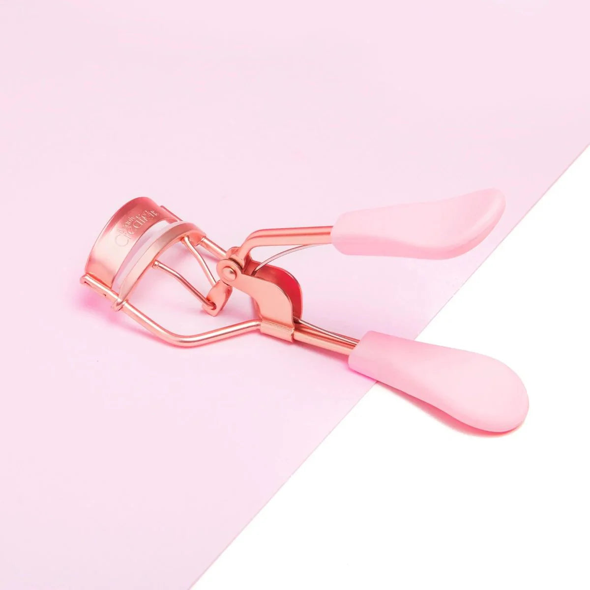 Rose gold and pink eye curler on a pink background